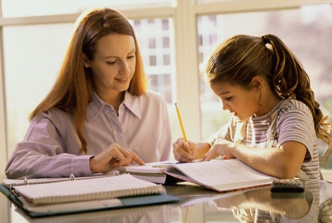 A tutor sits at a table and points to an open textbook.